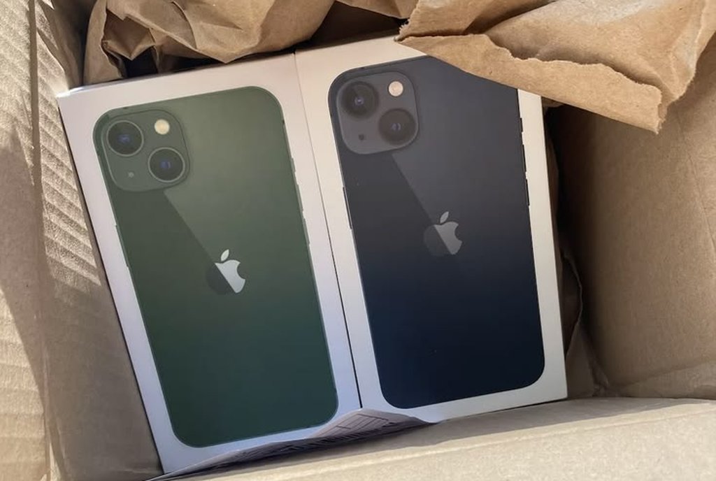 Caixa de papelão com dois celulares lacrados, um verde e um preto, sobre papel pardo