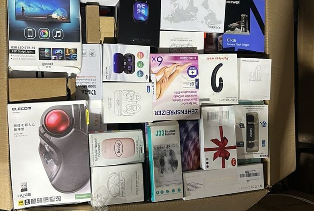 Vista de cima de uma caixa de papelão cheia de pequenos eletrônicos e acessórios ainda lacrados